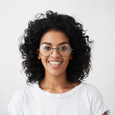 Portrait of positive carefree dark-skinned girl dressed casually smiling broadly, posing isolated at studio wall, having happy joyful look, relaxing indoors. Human facial expressions and emotions